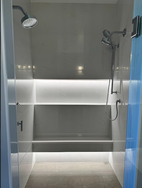 Modern shower with two showerheads, one fixed and one handheld, in a minimalist design with white marble walls.
