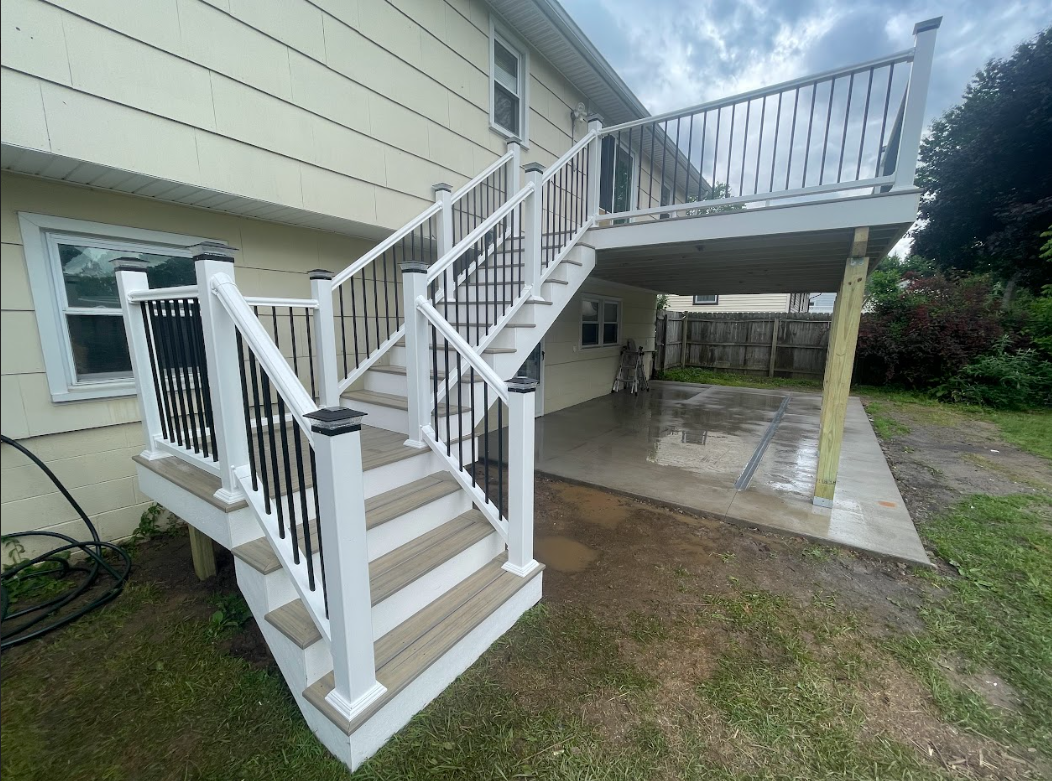 Backyard with a newly built two-level deck attached to a house, with stairs leading to the lower level and a covered upper level, on a cloudy day.
