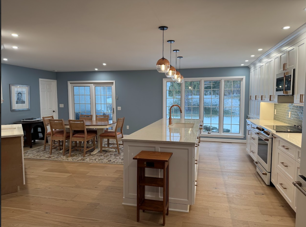 Open-concept kitchen and dining area with large window overlooking snowy landscape, white cabinets, island with sink, and wooden dining table with chairs.