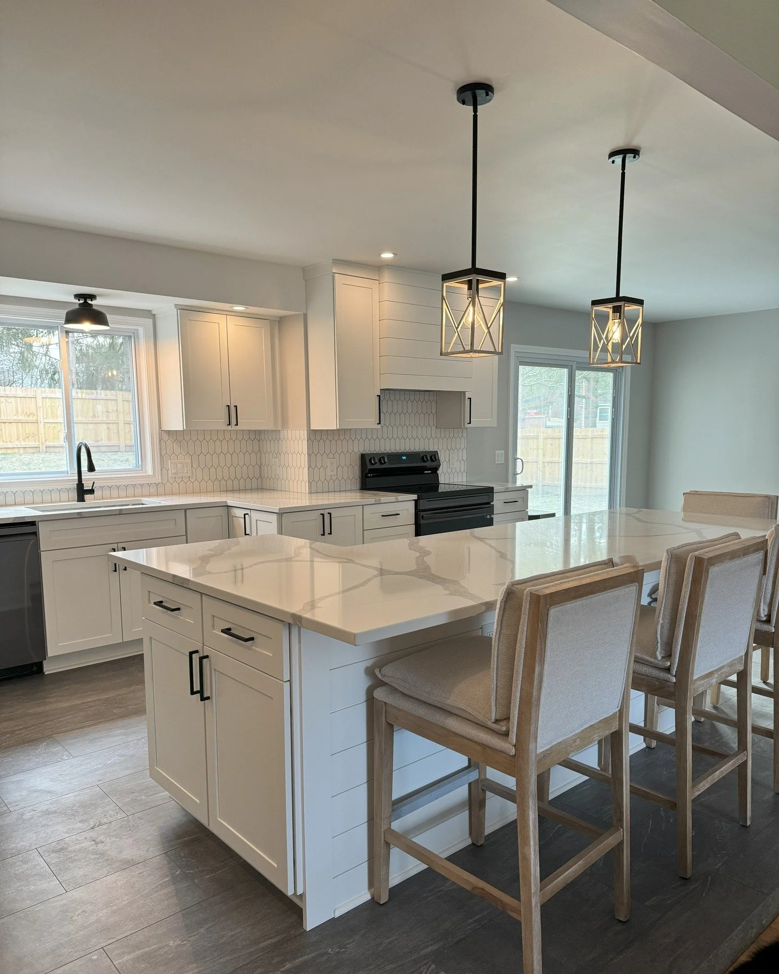 Modern kitchen with white cabinets, a marble island, black appliances, pendant lights, and beige barstools.