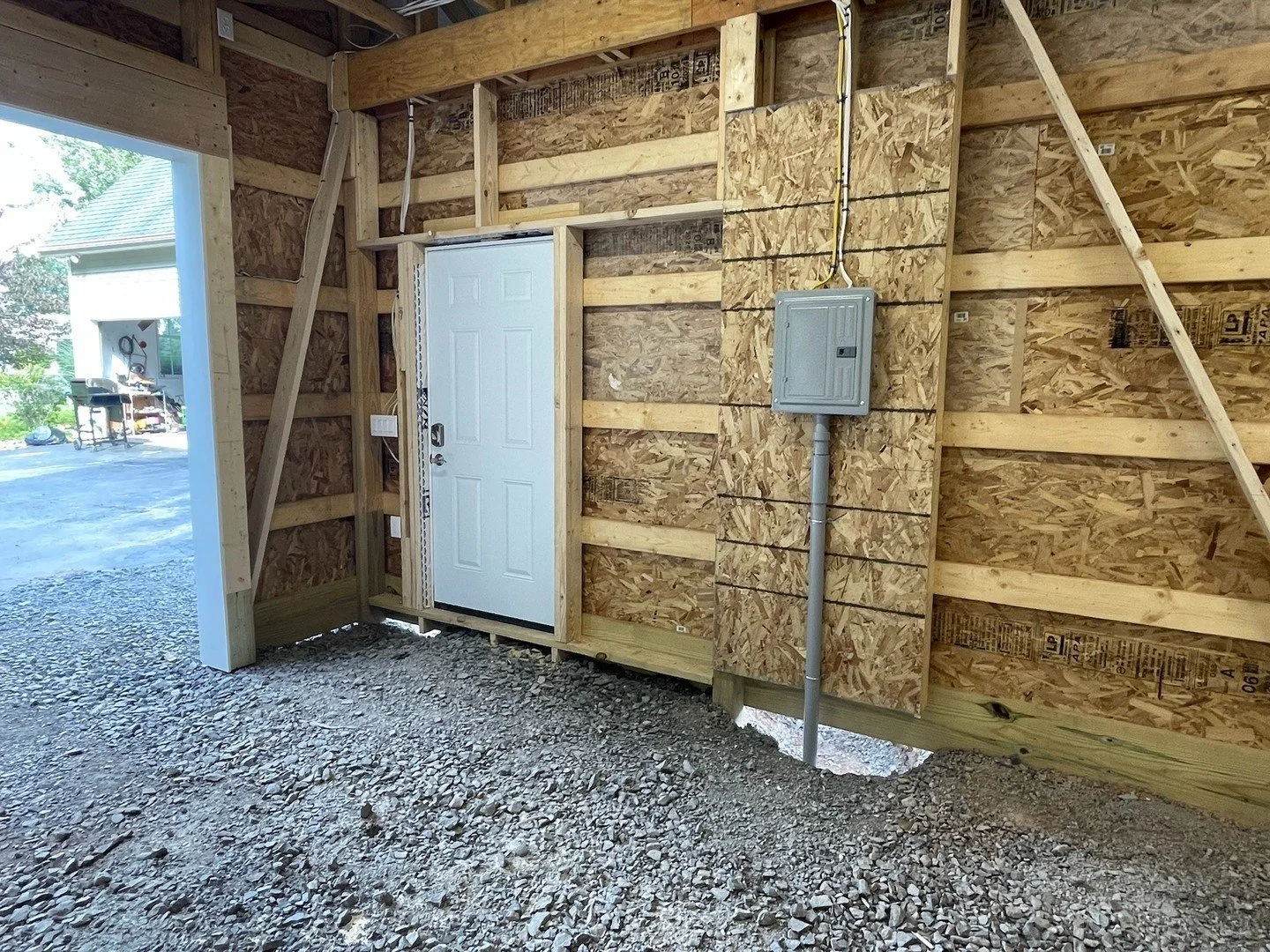 Interior view of a wooden structure under construction with a white door, electrical box, and wiring visible on the wall.