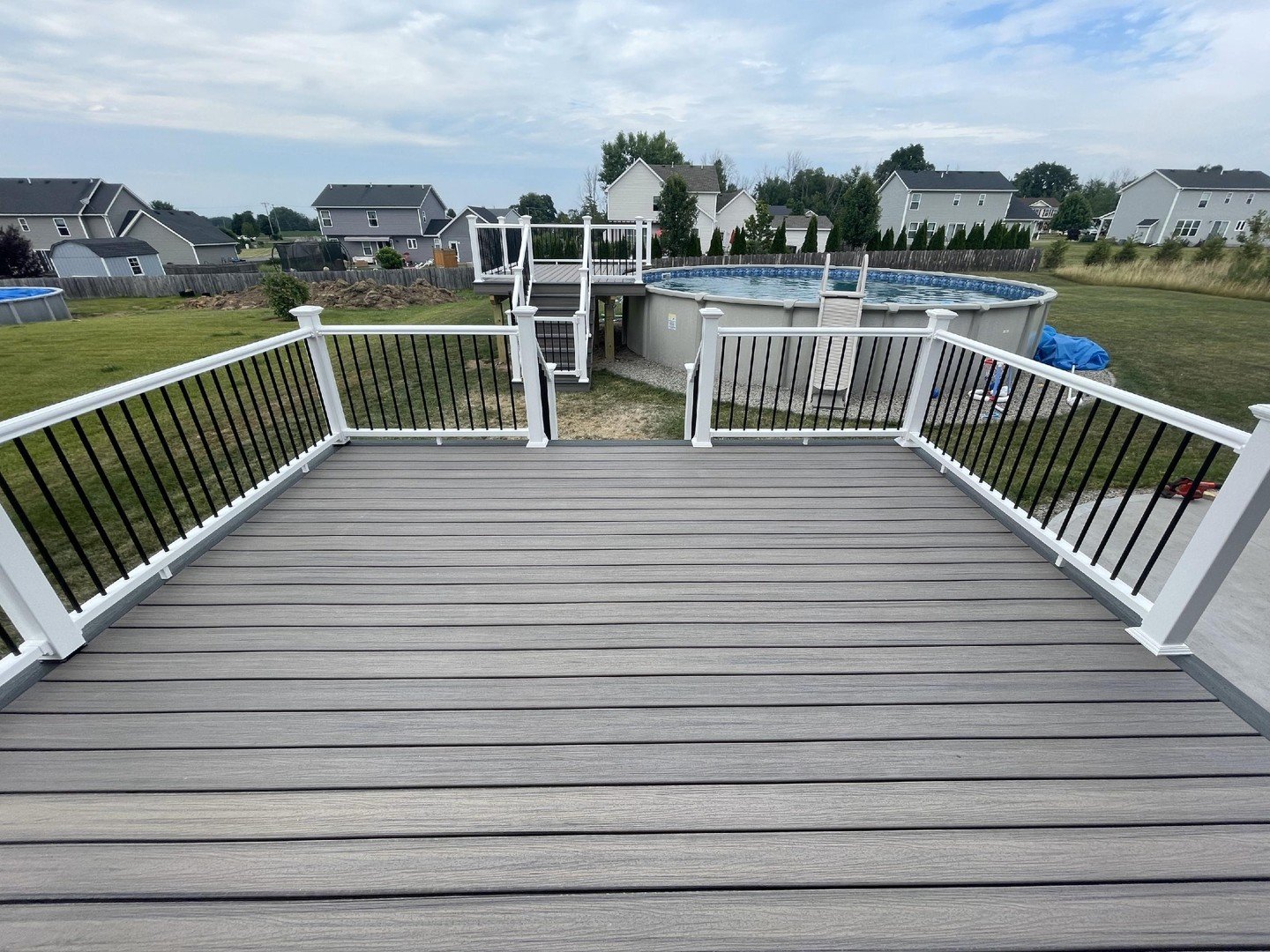 View from a wooden deck overlooking a backyard with a above-ground swimming pool and neighboring houses.