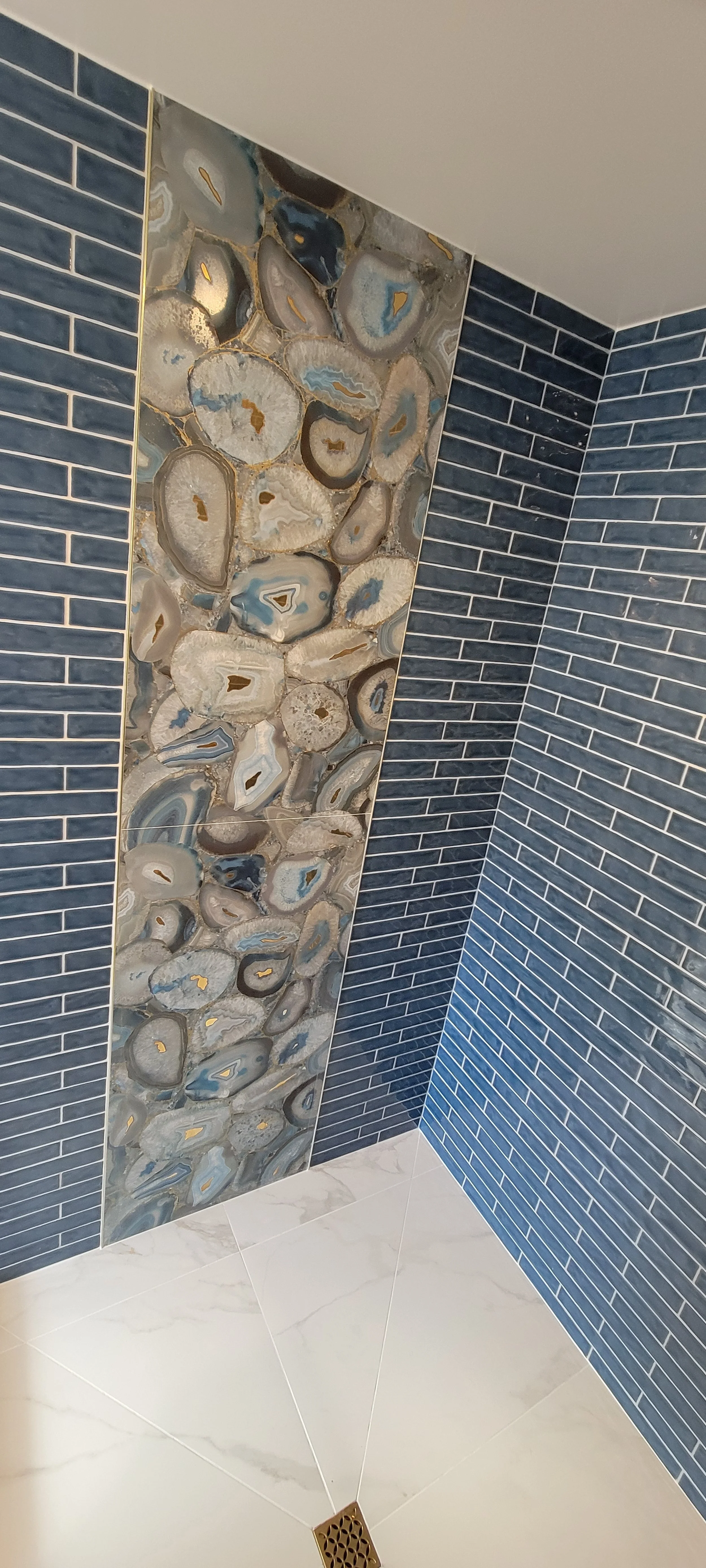 Bathroom corner with blue subway tile walls, a vertical strip of geode-style tiles, and a white floor with a drain.