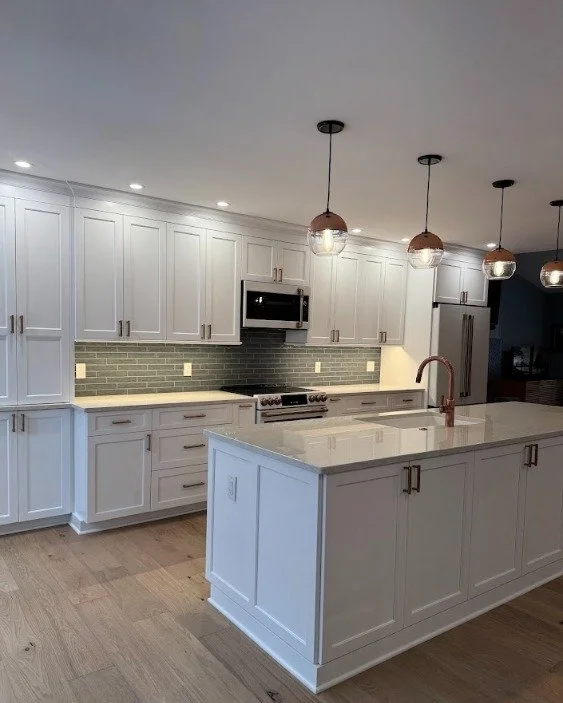 Modern kitchen with white cabinets, a white island with a copper faucet, a black stove, built-in microwave, and pendant lights hanging above the island.