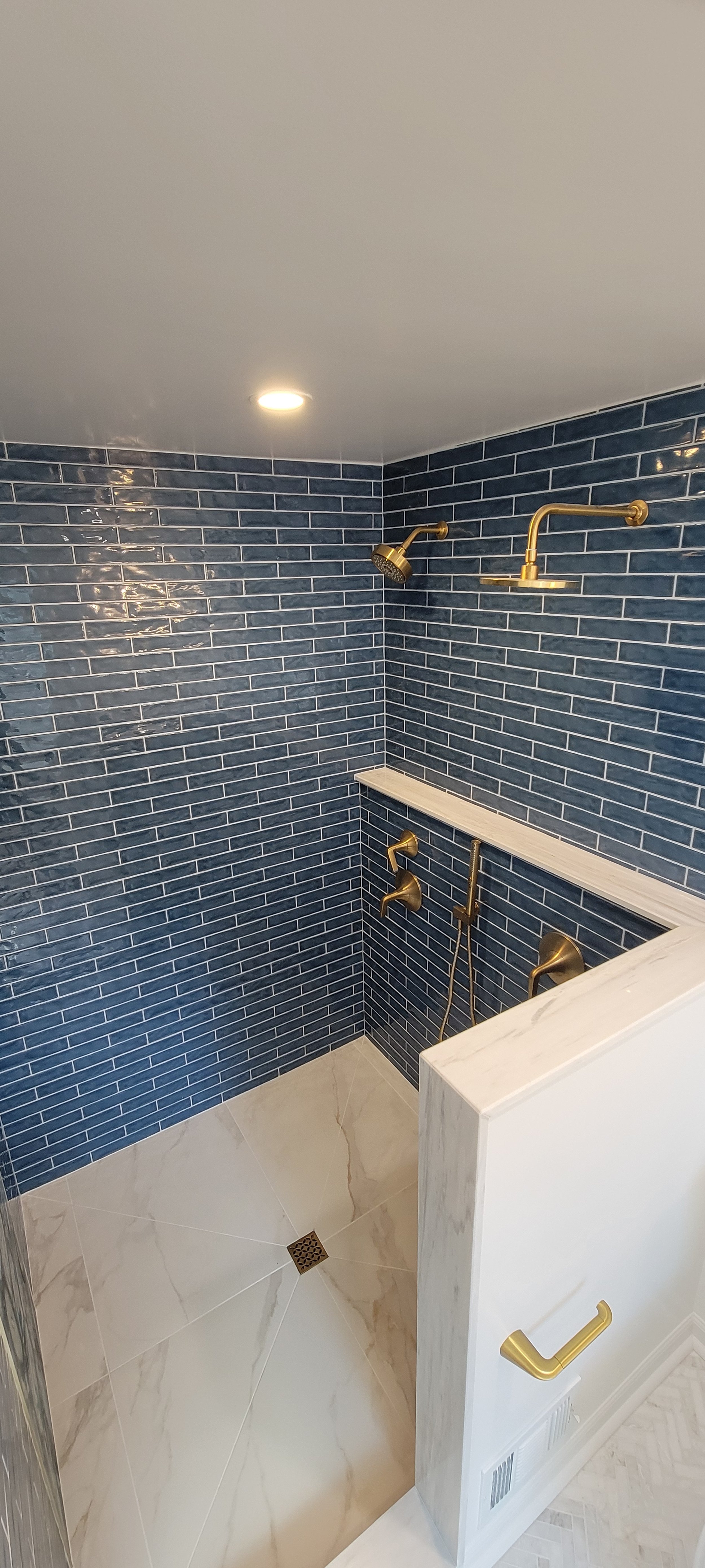 Bathroom shower area with dark blue subway tiles, gold fixtures, and a marble shelf.