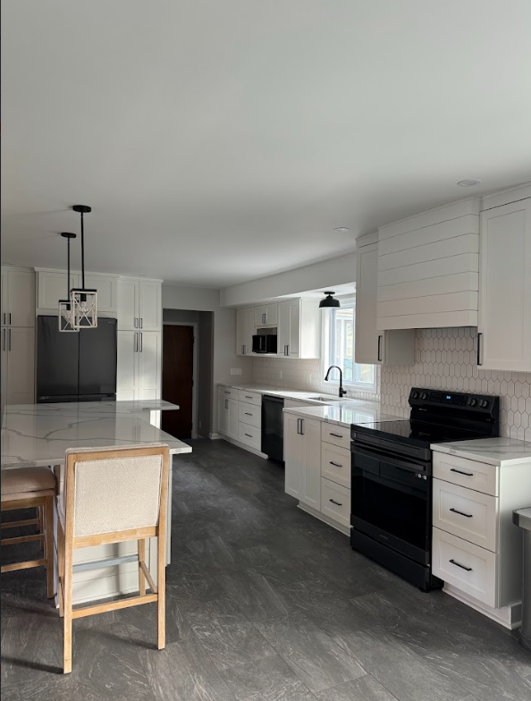 Modern kitchen with white cabinets, black appliances, gray flooring, and a kitchen island with seating.