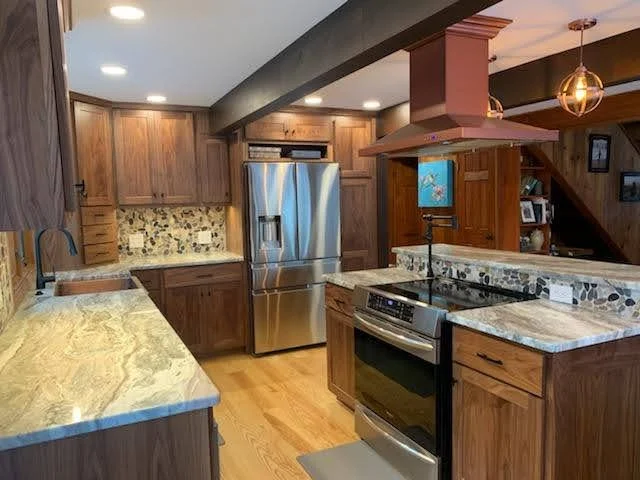 Kitchen with wooden cabinets, stainless steel refrigerator, granite countertops, and a stove with a vent hood.