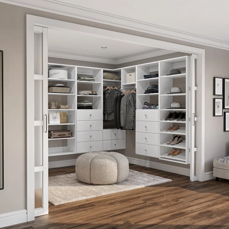 A walk-in closet with organized shelves and drawers, containing folded clothes, hanging garments, shoes, and hats, with a plush ottoman in the center.