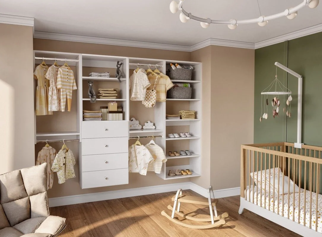 Nursery room with a wall open closet containing clothes, shoes, andStorage bins, a wooden crib, a white rocking chair, and a digital baby monitor hanging from a mobile arm.