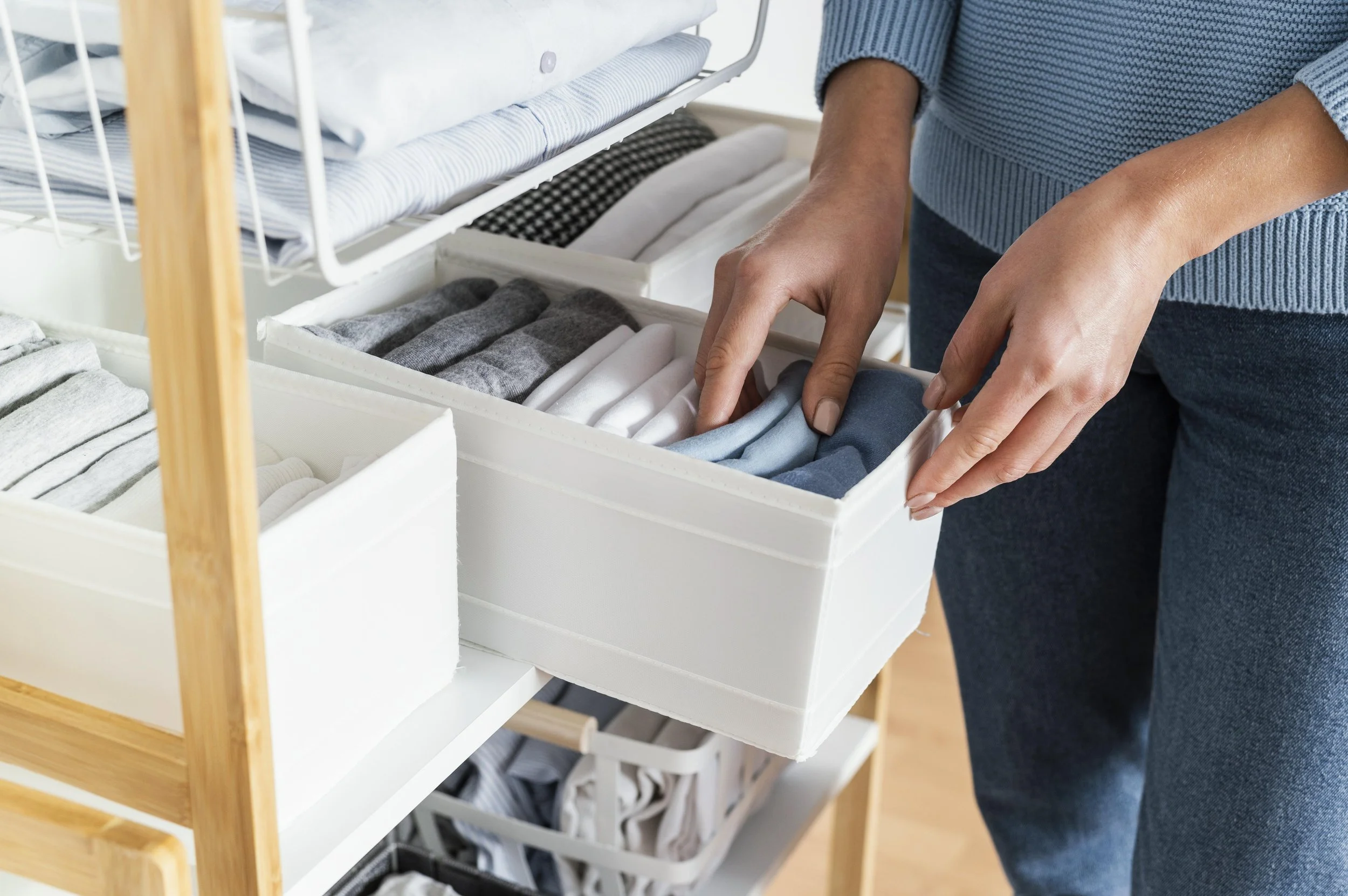 Hands placing folded clothes into a fabric storage bin for an organized closet system.