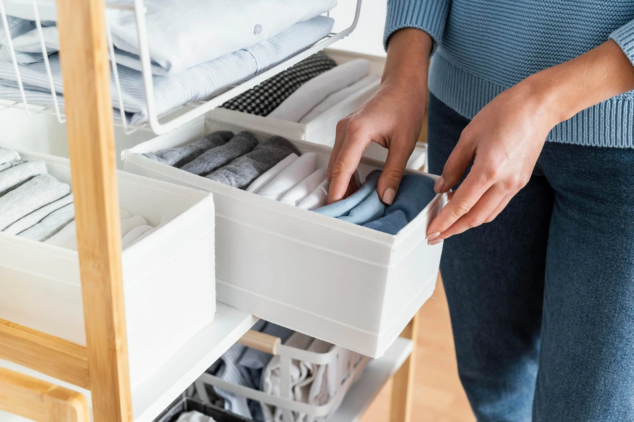 Hands placing folded clothes into a fabric storage bin for an organized closet system in the DMV area.