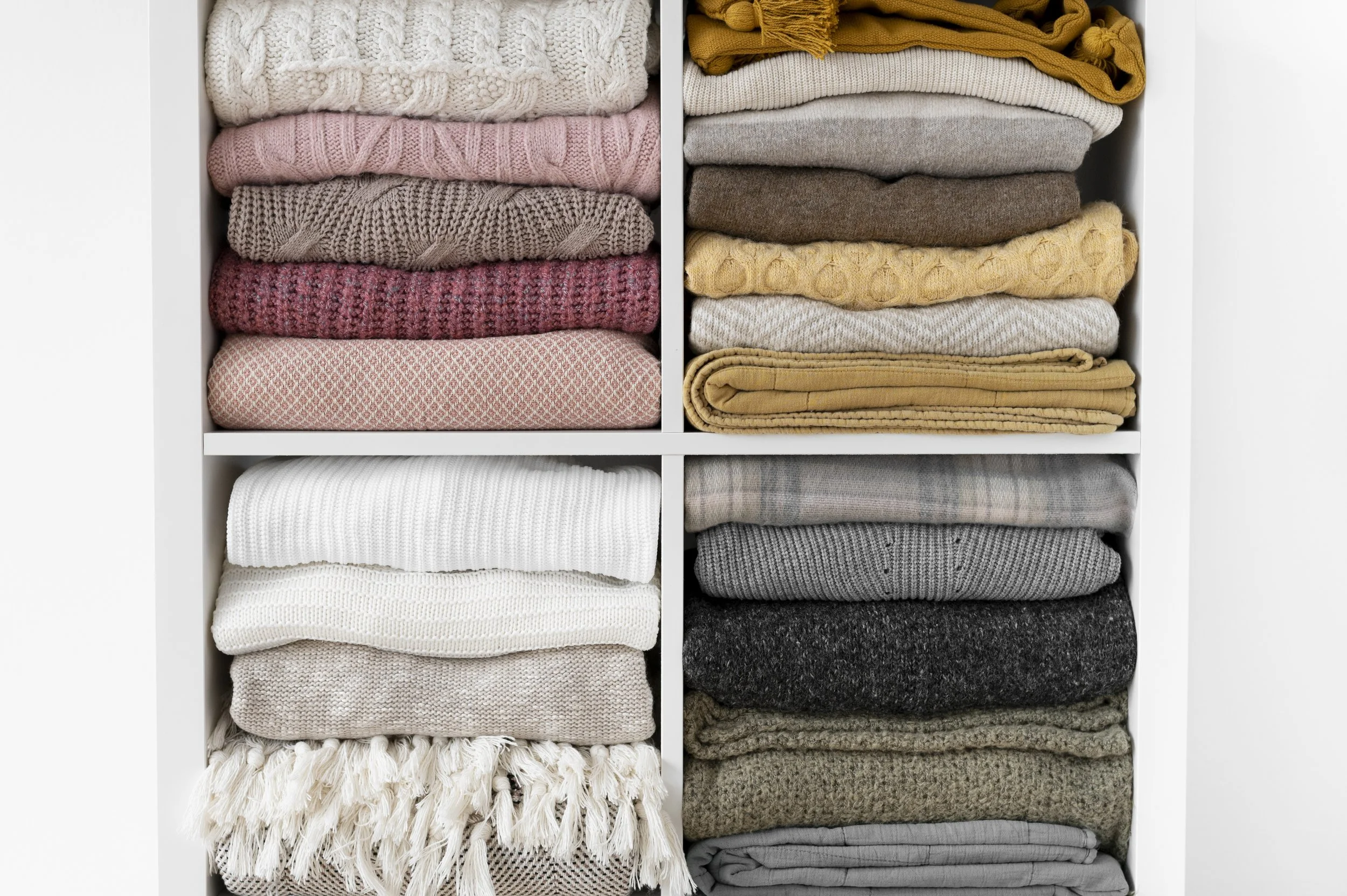Organized closet with folded sweaters on white shelves.