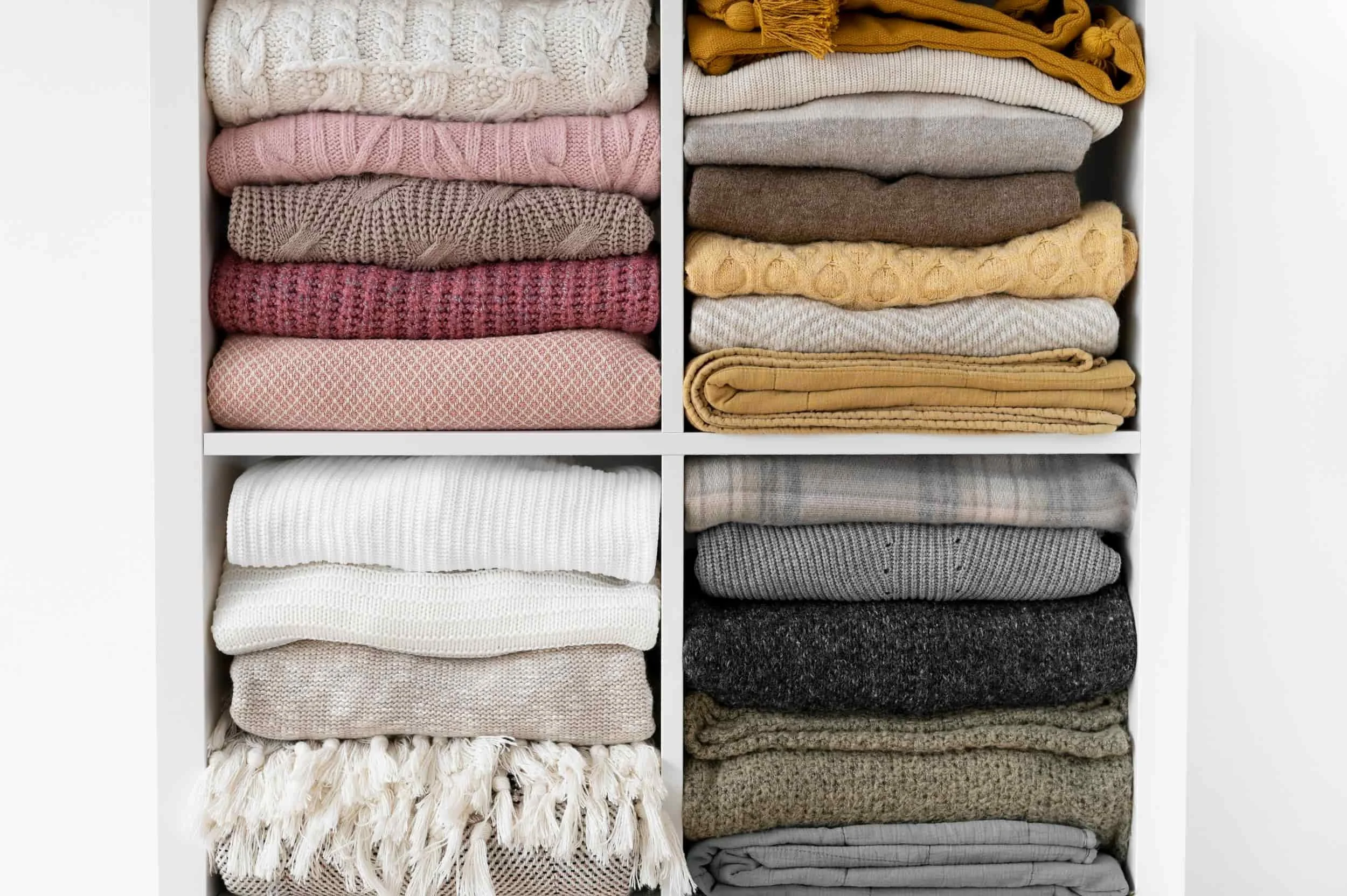 Organized closet with folded sweaters on white shelves.