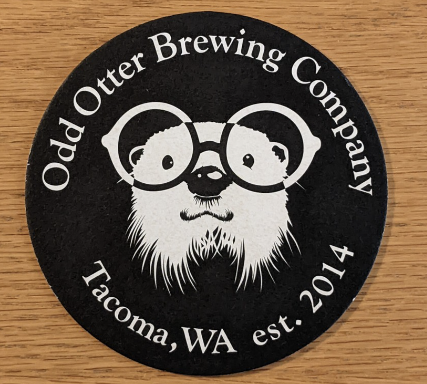 Round black and white coaster with a beaver wearing glasses, surrounded by text that reads "Odd Otter Brewing Company, Tacoma, WA, est. 2014."