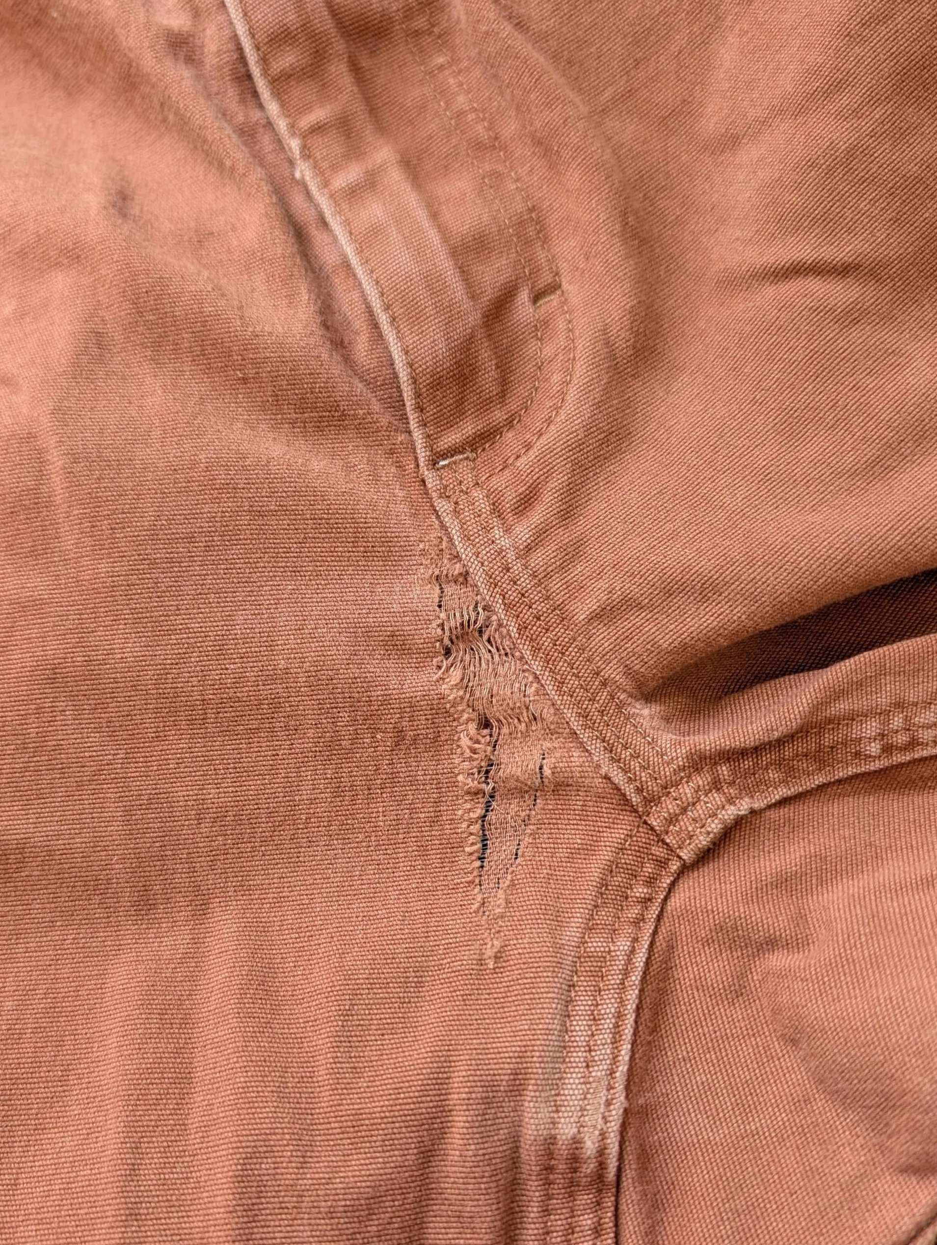 Close-up of a pair of worn, distressed brown pants with a tear near the seam.