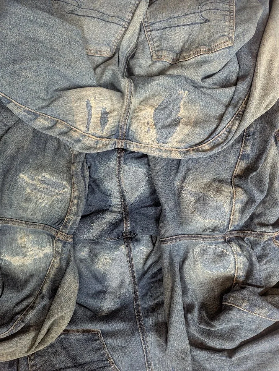 A pile of worn and torn blue denim jeans with faded and distressed areas.