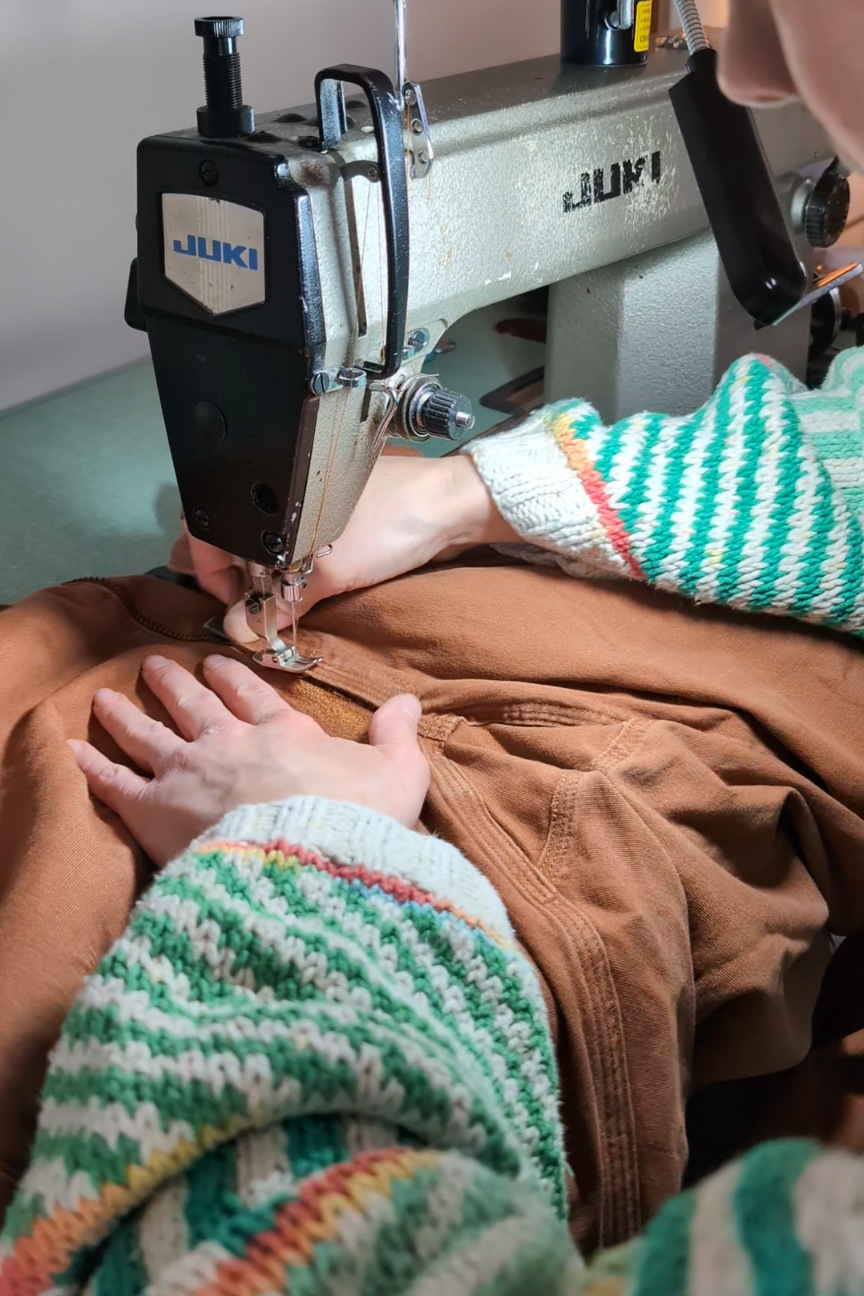A person sewing brown fabric with a Juki industrial sewing machine, wearing a colorful striped sweater.