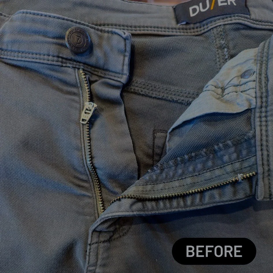 Close-up of the top part of a pair of gray pants with the zipper partially open, showing the button and waistband details.