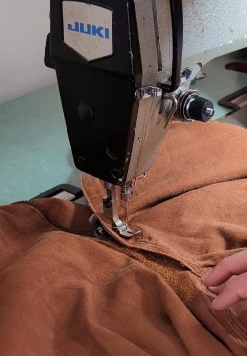 Close-up of a Juki industrial sewing machine sewing a brown fabric.