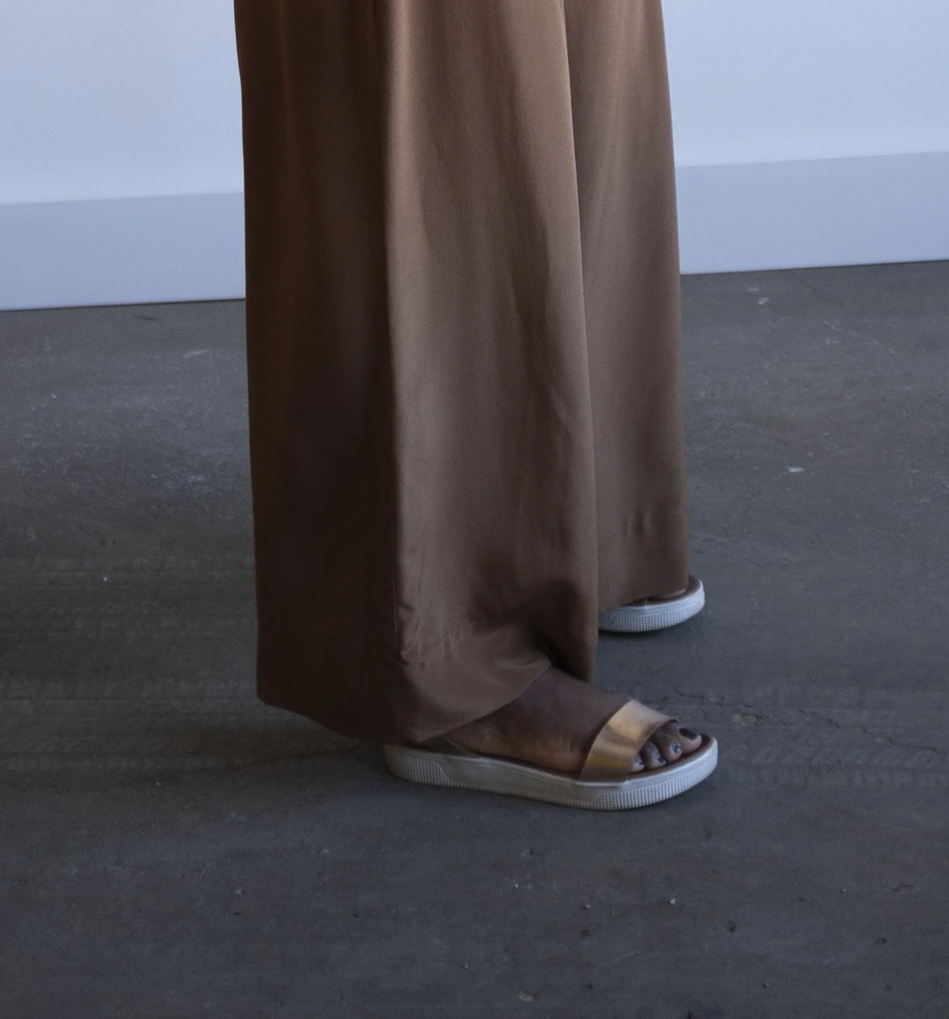 Person wearing brown wide-legged pants and open-toe sandals standing on a concrete floor.