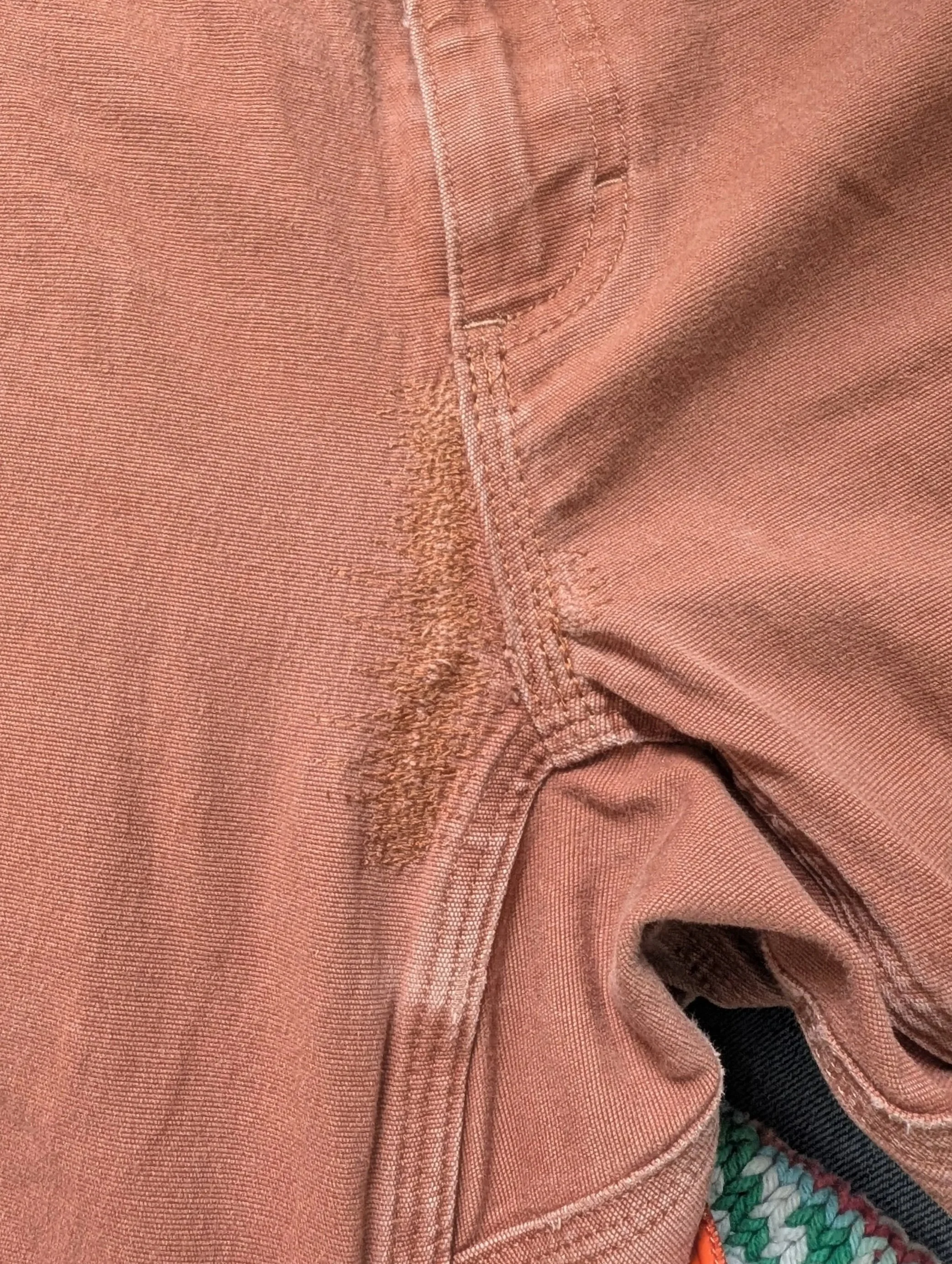 Close-up of peach-colored denim jeans with visible stitching and frayed area near pocket.