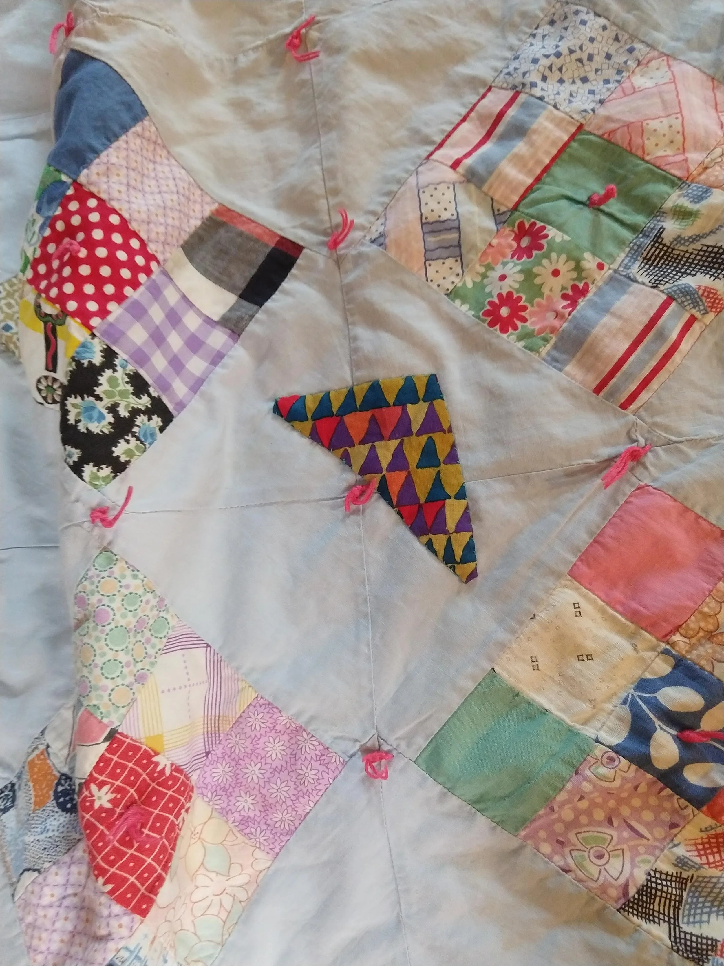 Close-up of a quilt with a central colorful triangular pattern surrounded by patches of various fabric prints.