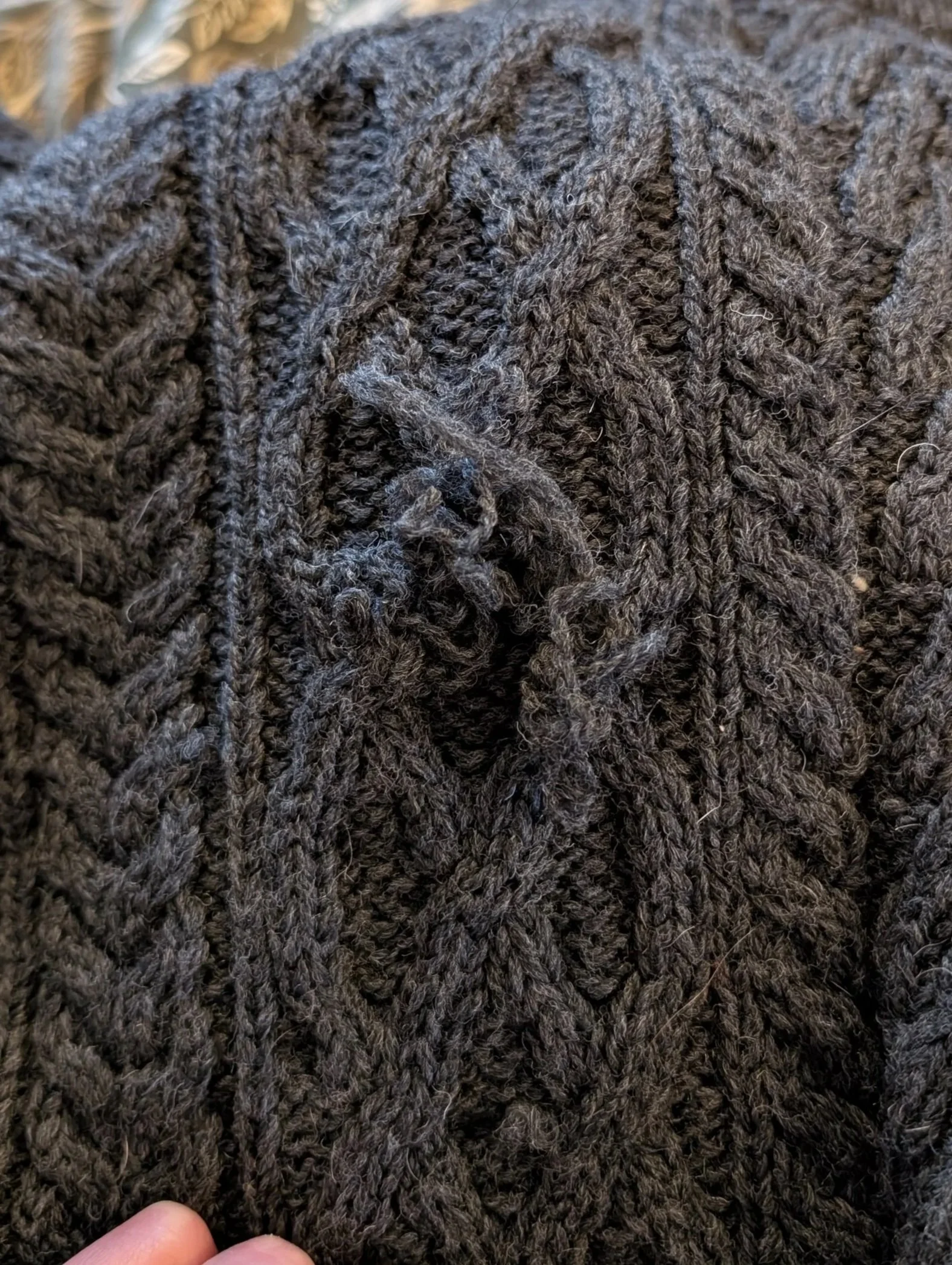 Close-up of a dark-colored knitted fabric with a cable knit pattern and some loose fibers.