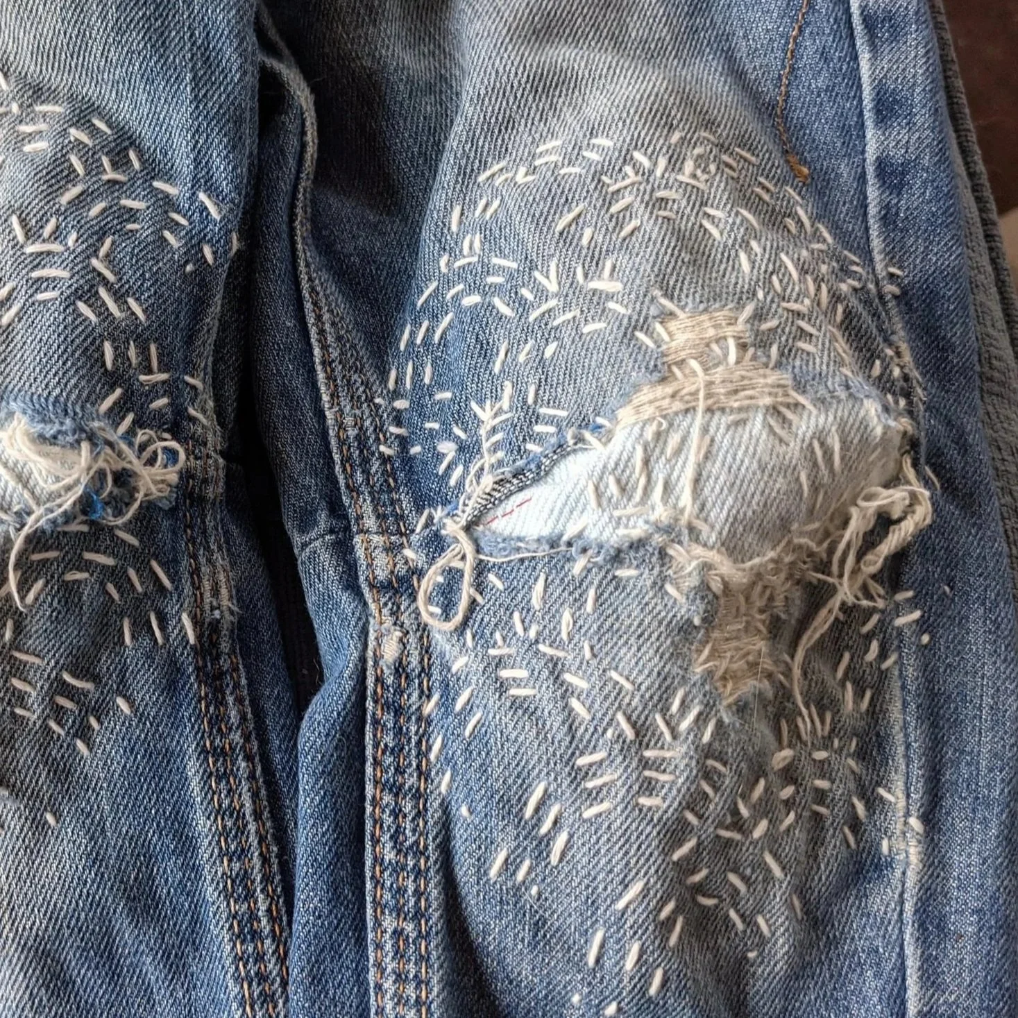Close-up of torn and distressed denim jeans with decorative white embroidery or stitching.