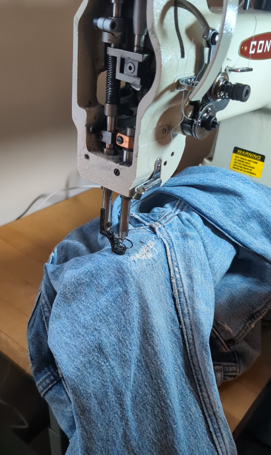A sewing machine stitching denim jeans on a wooden table.