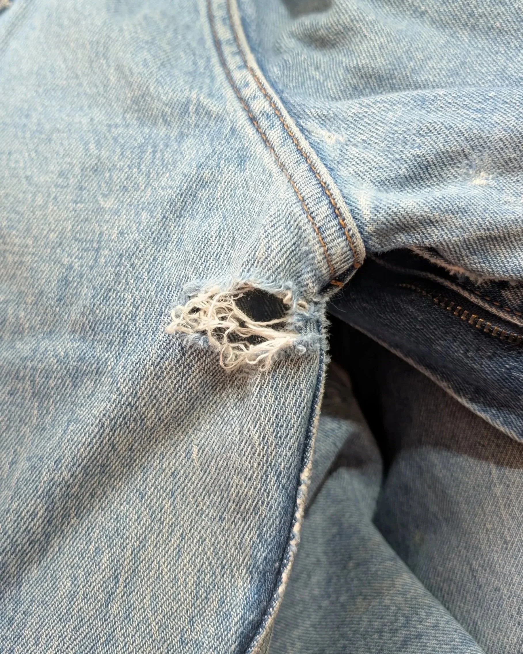 Close-up of distressed light blue denim jeans with a tear near the thigh.