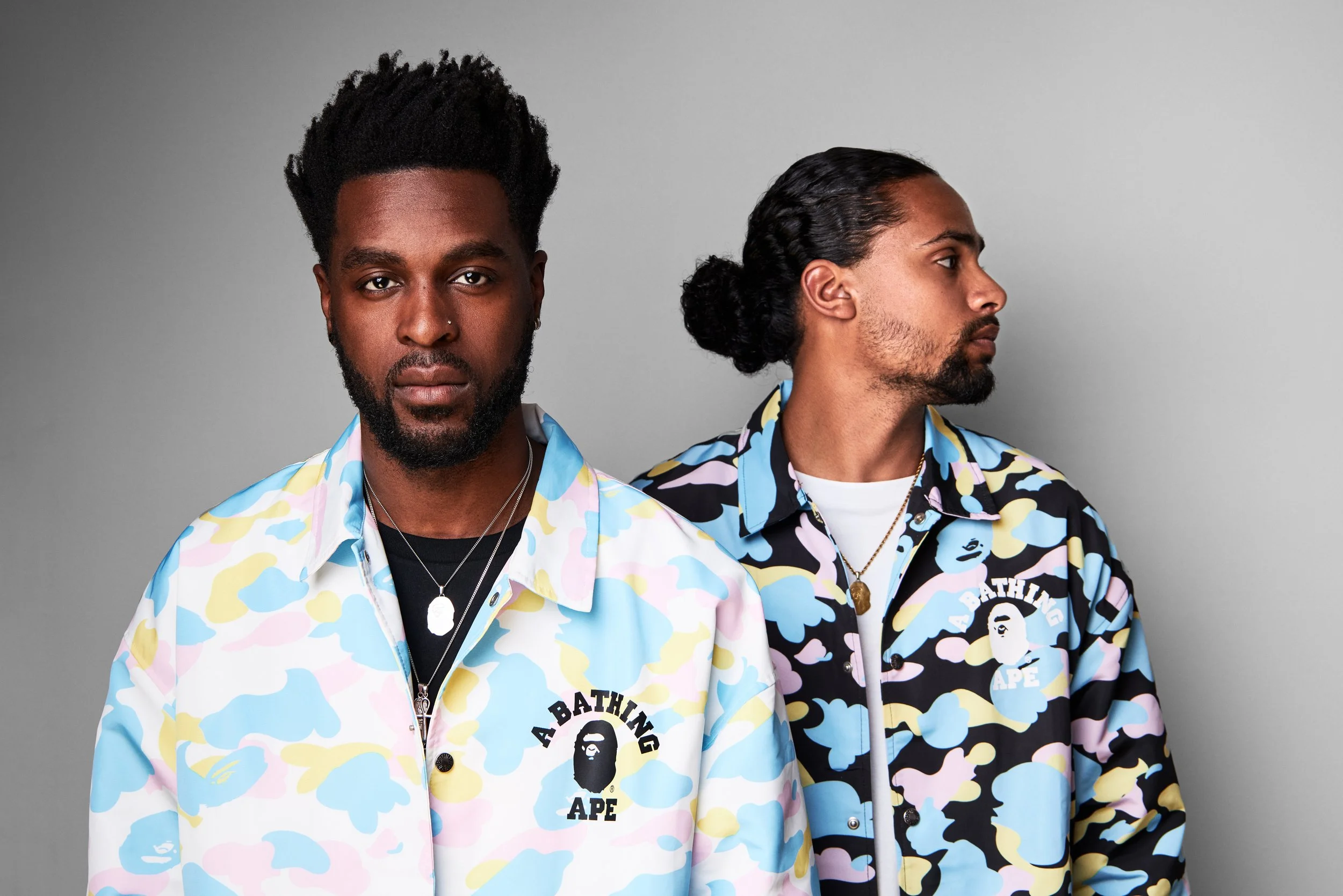 Two men with camo shirts featuring Bape logo standing against a gray background, one facing forward and the other in profile.
