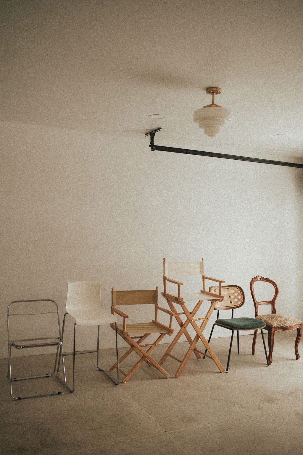 Five chairs of various styles lined up against a plain wall in a room with a beige carpet.