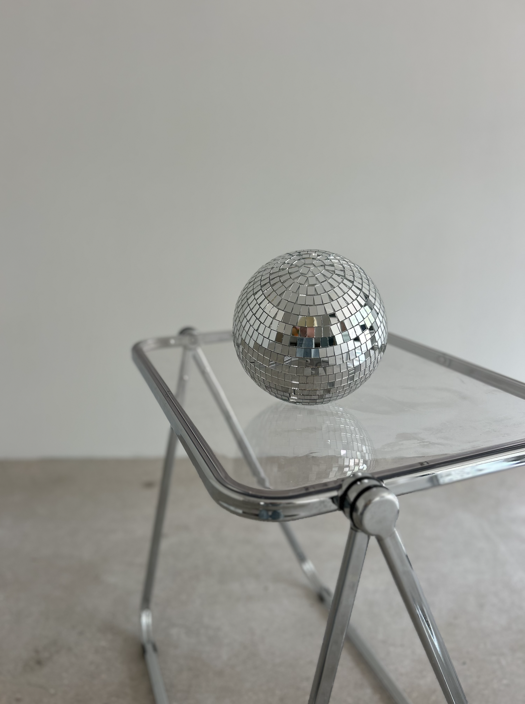 A small disco ball resting on a transparent glass-top table with metal legs.