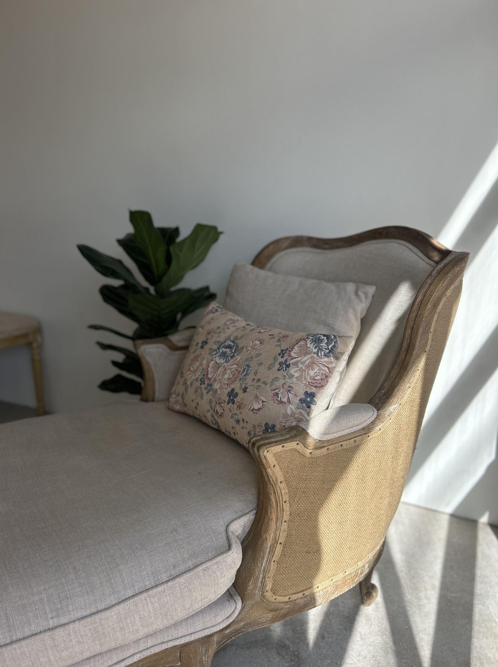 A vintage beige upholstered sofa with a wooden frame, featuring decorative pillows and a green plant in the background.
