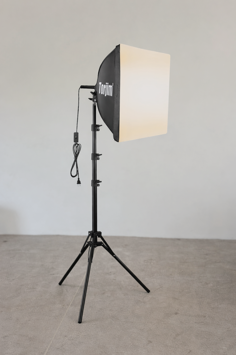 Photographic studio softbox light on a black adjustable stand in an empty room with plain gray walls and concrete floor.