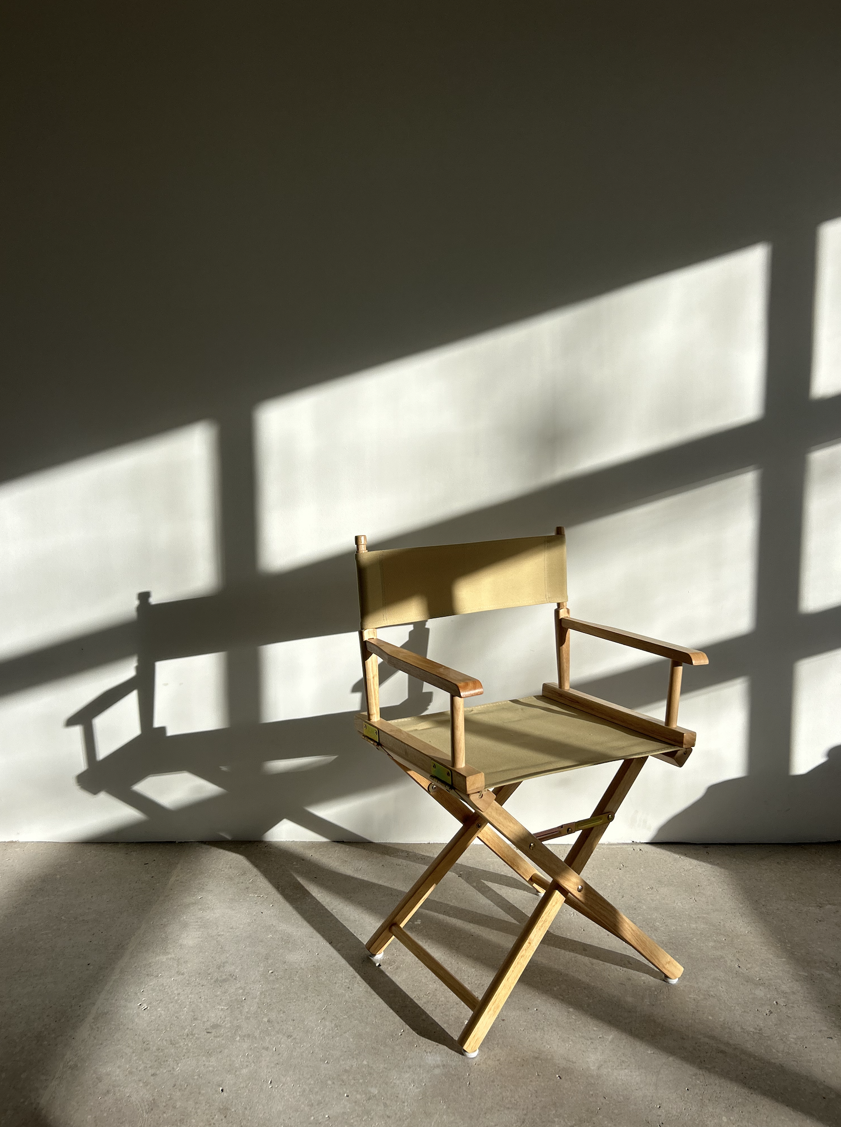 Empty director's chair against a white wall, with sunlight casting geometric shadows.