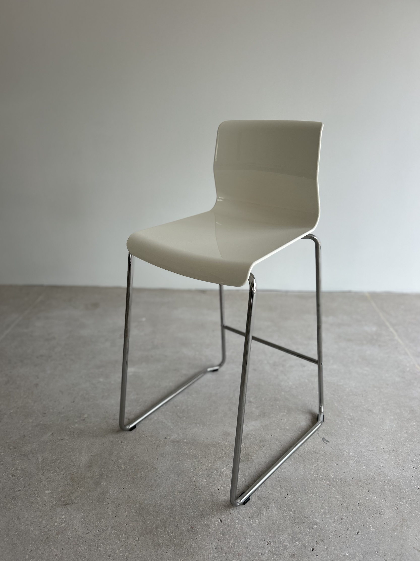 Modern white chair with chrome legs placed on a concrete floor against a plain wall.