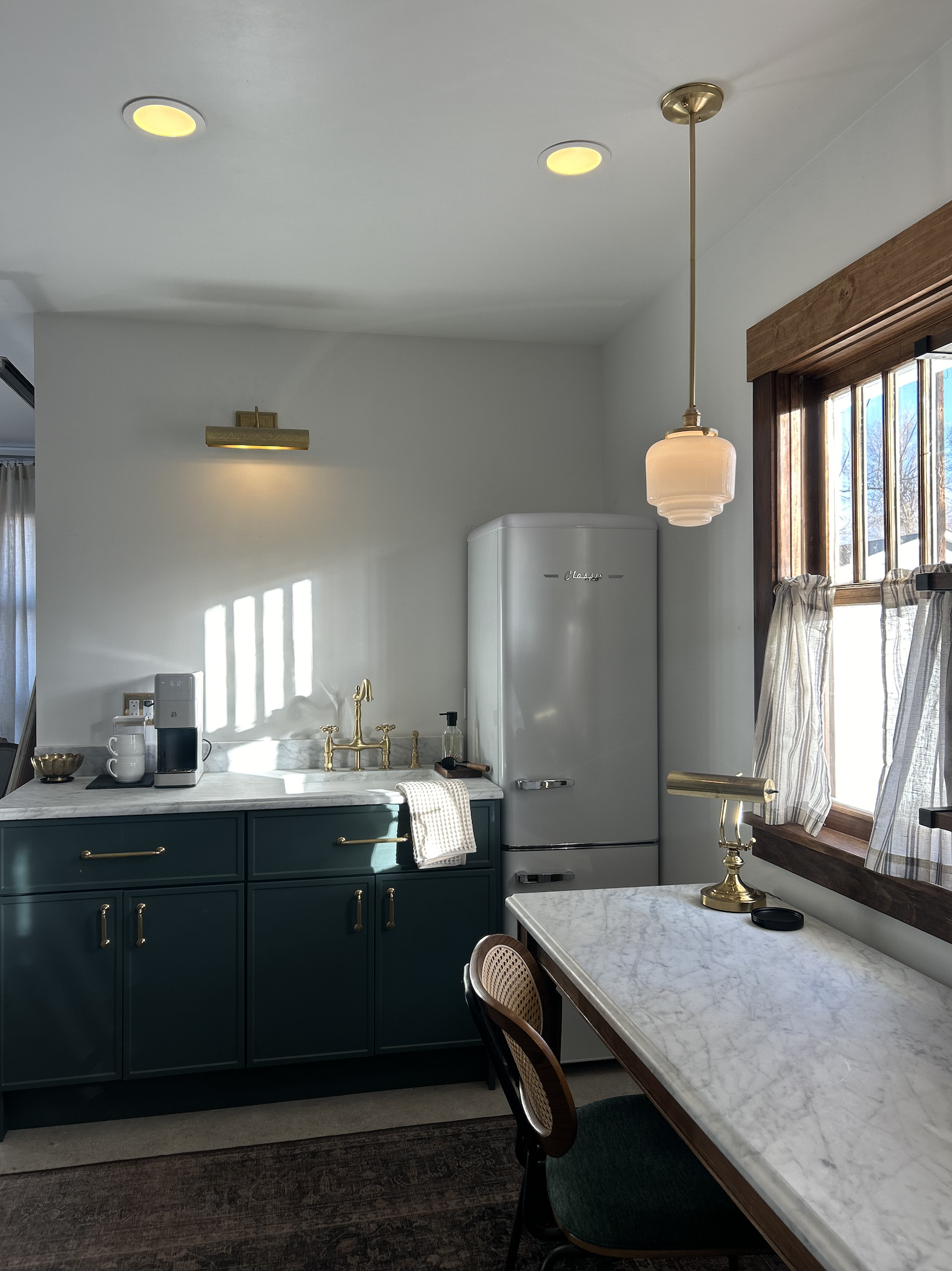 Kitchen with green cabinets, marble countertop, retro refrigerator, gold fixtures, and a window with curtains.