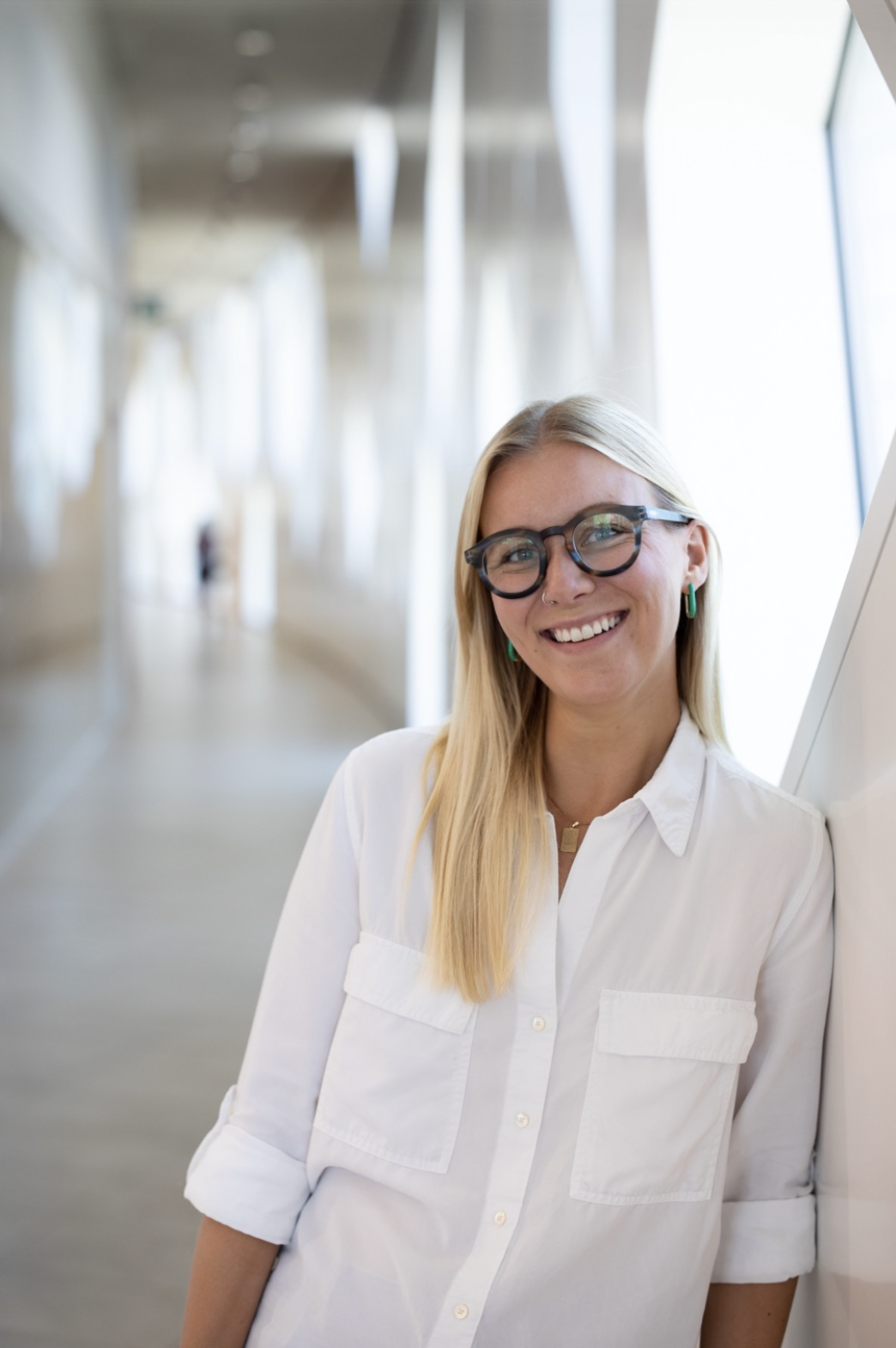 A woman with blonde hair, glasses, and a white shirt smiling in an airport corridor.