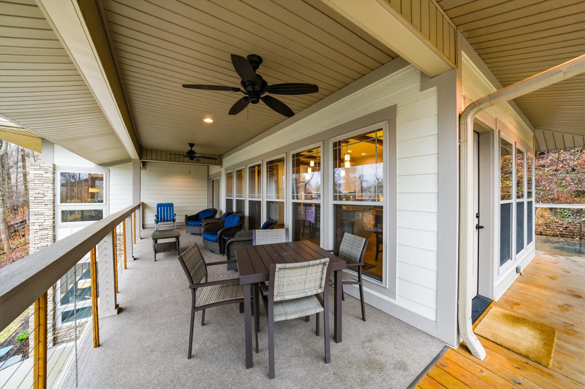 Covered balcony with chairs, a table, ceiling fans, and a view of trees outside.