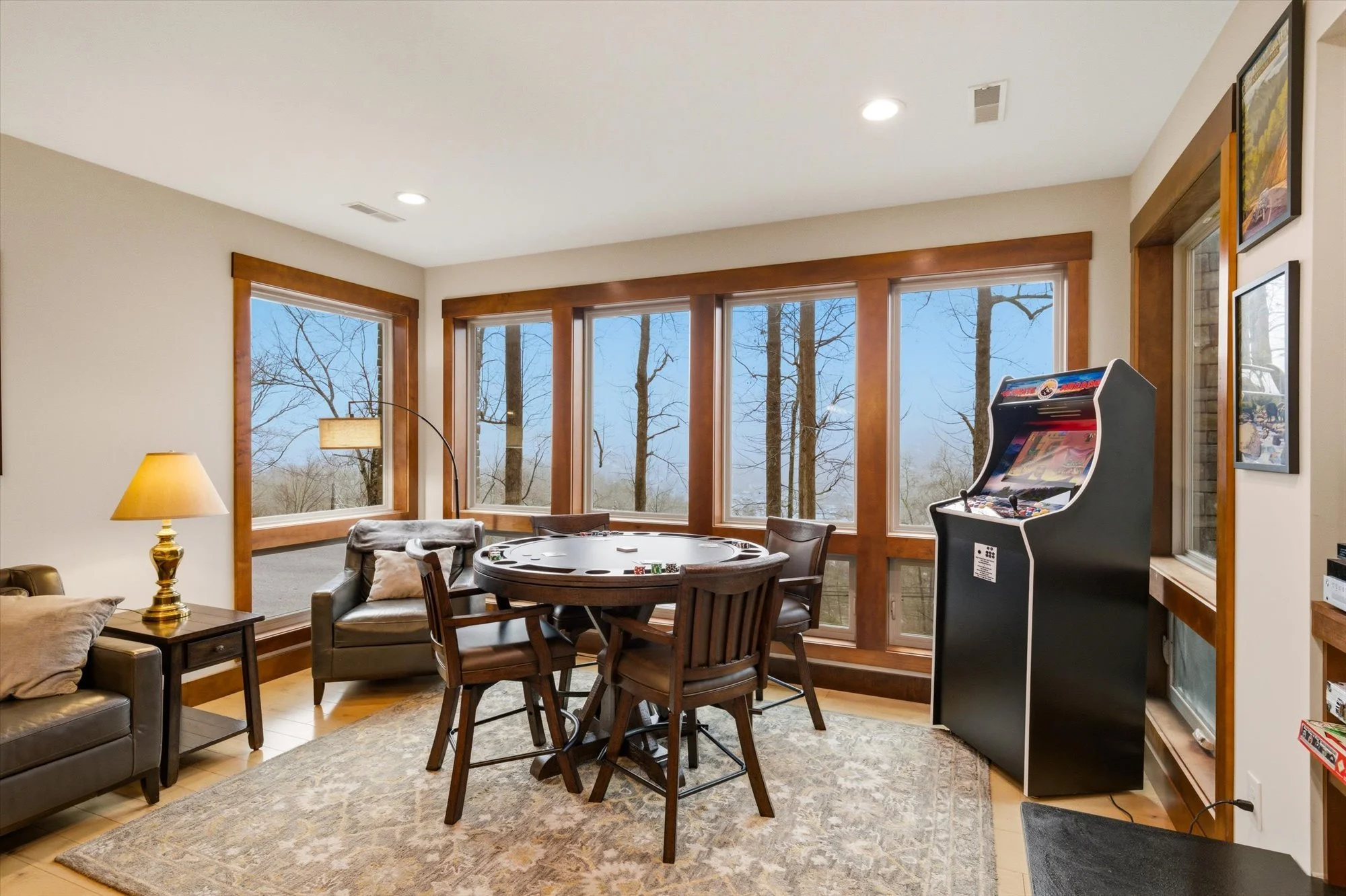 Living room with large windows, poker table, arcade game, sofa, side table, lamp, and framed pictures.