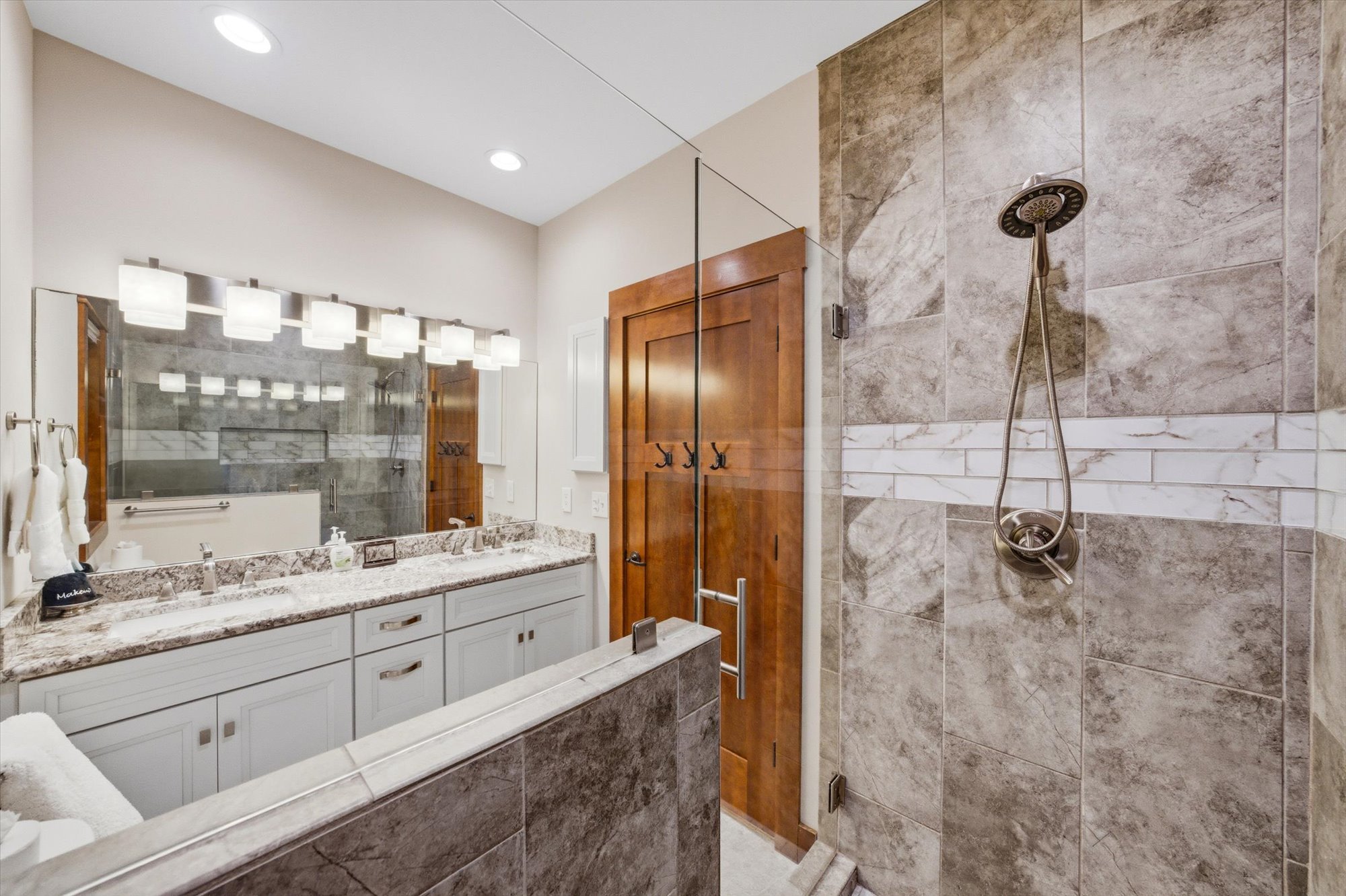 Modern bathroom with a marble vanity, large mirror, glass shower enclosure, and a rain shower head.