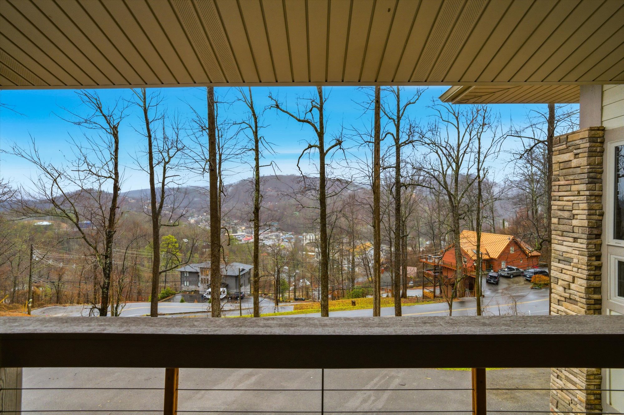 View from a balcony showing leafless trees, a parking lot, and houses with hills in the background on a clear day.