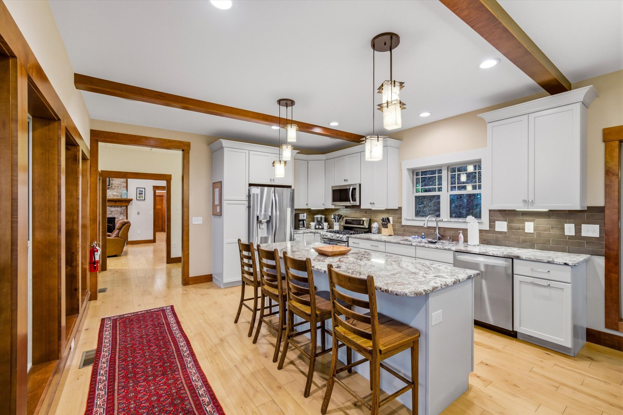 Modern kitchen with white cabinets, granite countertops, stainless steel appliances, wooden bar stools, hardwood flooring, and hanging pendant lights.