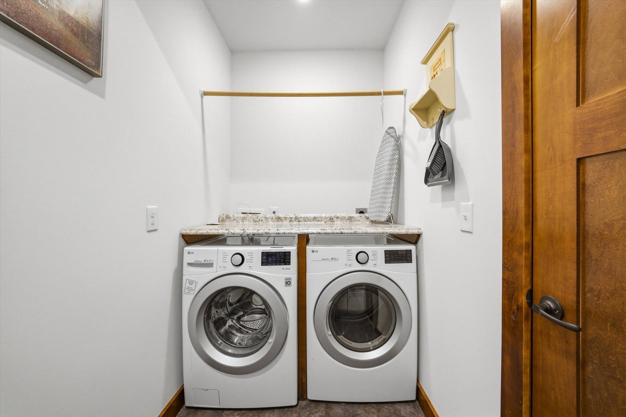 Laundry room with white LG washer and dryer, granite countertop, ironing board, and wall hooks for cleaning supplies.