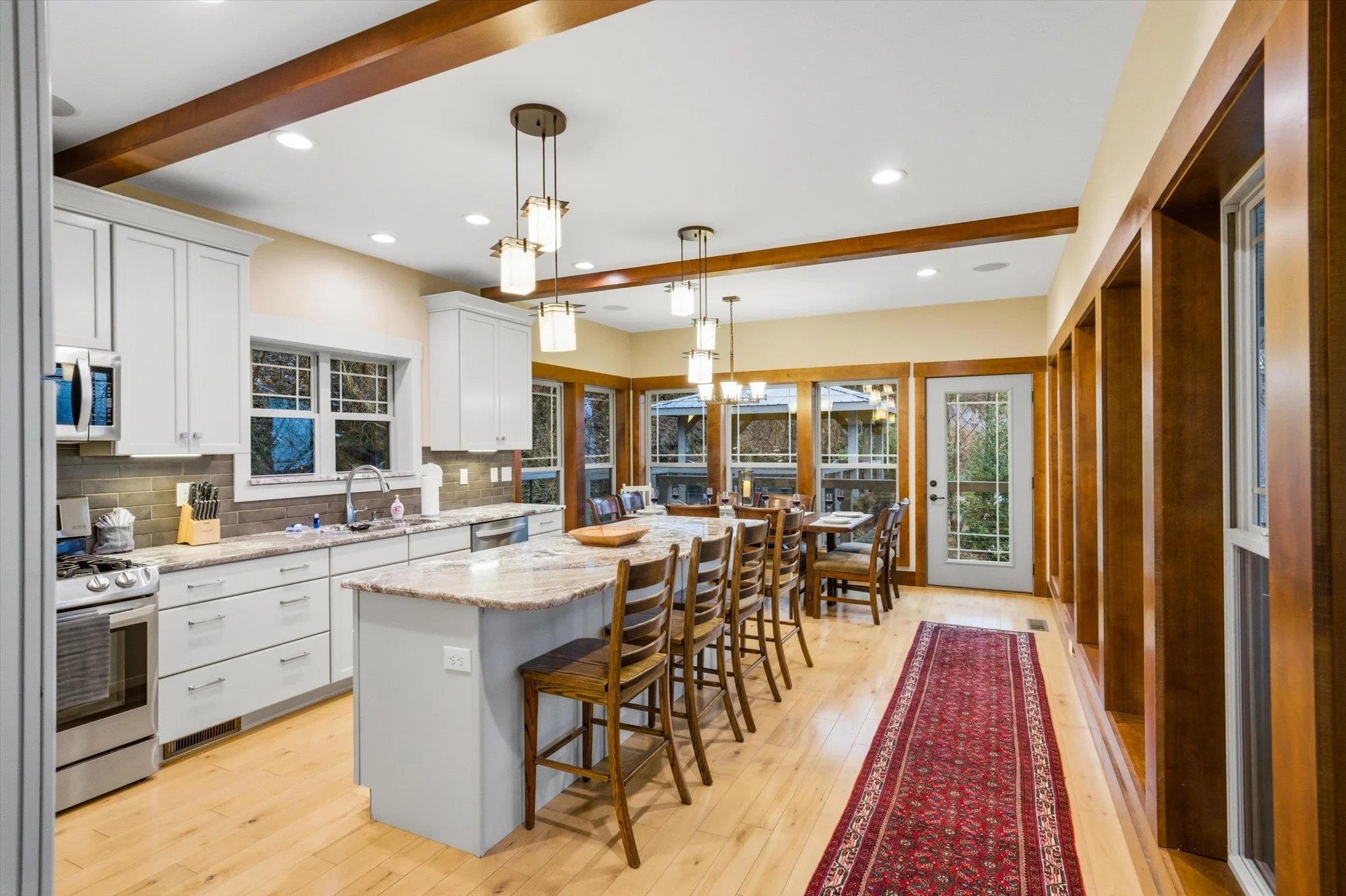 Clean kitchen with white cabinets, granite countertops, stainless steel appliances, wood flooring, and a dining table with chairs near large windows and a door leading outside.