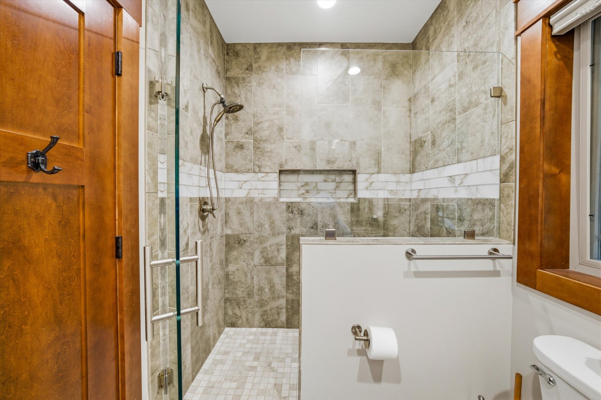 Bathroom with tiled walk-in shower, wooden walls, privacy window, toilet with toilet paper, and recessed shelf in shower