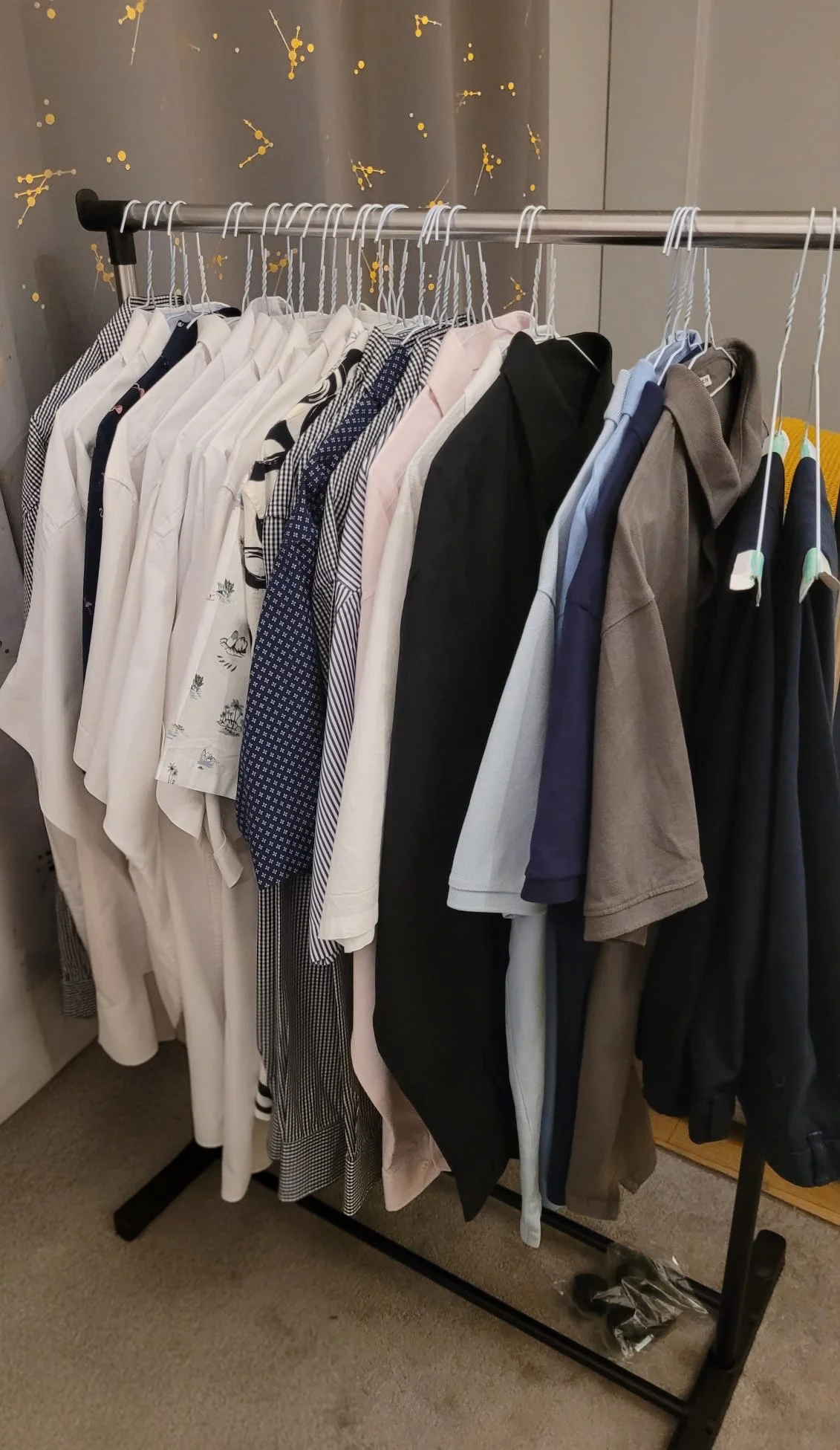 A clothing rack with various shirts and tops in neutral and dark colors on hangers.