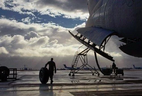 A person walking with a tire near an airplane on the tarmac at an airport.