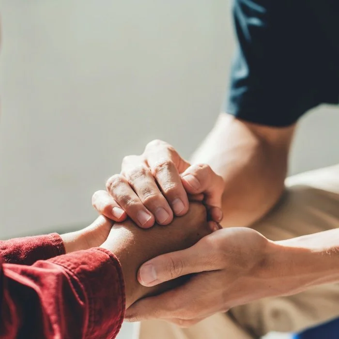 Two people clasping hands, one comforting the other.